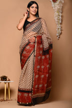 Woman wearing a traditional saree with a beige and red pattern against a beige background